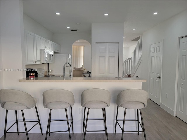 kitchen with a kitchen breakfast bar, white cabinetry, white appliances, light wood-style floors, and a peninsula