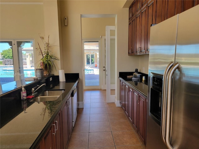 kitchen featuring light tile patterned floors, baseboards, a sink, dishwasher, and stainless steel fridge