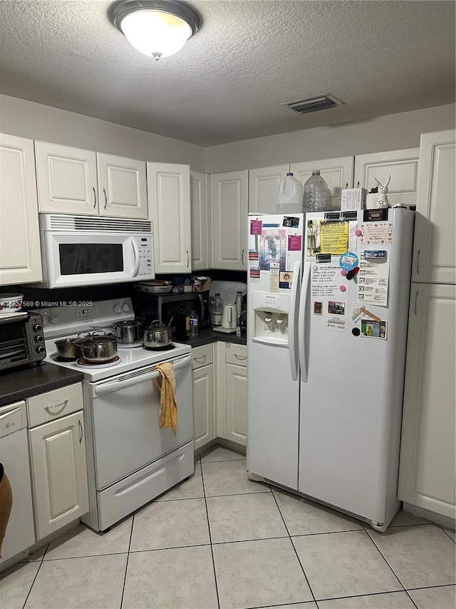 kitchen featuring white appliances, light tile patterned floors, visible vents, a textured ceiling, and dark countertops