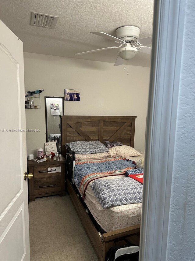 carpeted bedroom featuring visible vents, a textured ceiling, and a ceiling fan