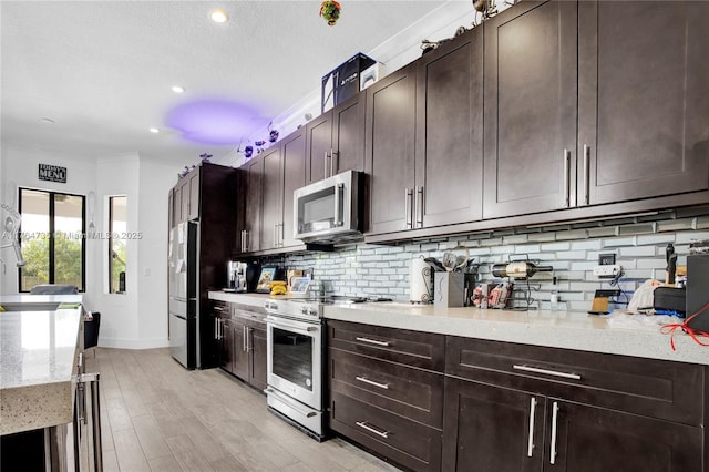 kitchen with light stone counters, light wood-style flooring, stainless steel appliances, dark brown cabinets, and backsplash