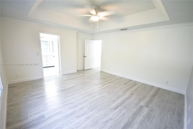 spare room featuring light wood-style flooring, a raised ceiling, and baseboards