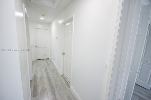 corridor with light wood-style flooring, baseboards, and a textured ceiling