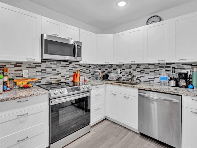 900 NE 195th St Unit 504, Miami, FL 33179 - kitchen with backsplash, light wood-style flooring, white cabinets, stainless steel appliances, and a sink