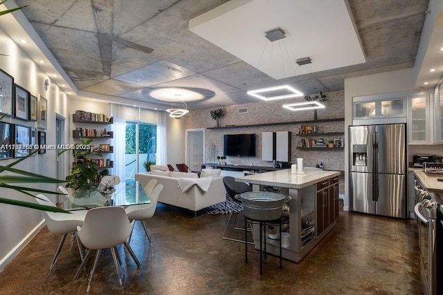 kitchen featuring a breakfast bar, open shelves, light countertops, concrete flooring, and stainless steel fridge