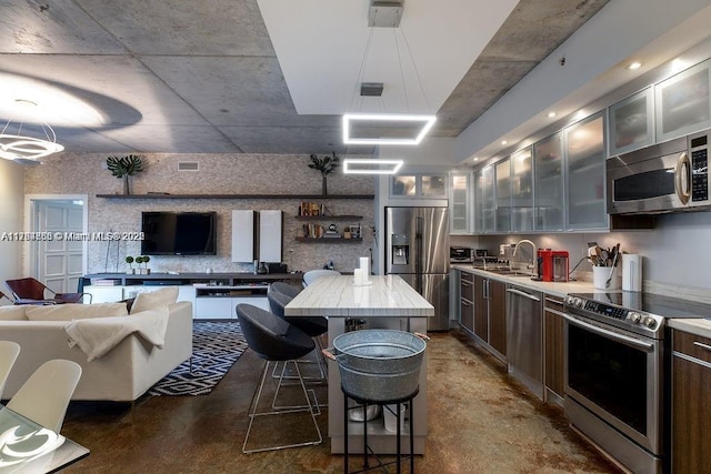 kitchen with a sink, appliances with stainless steel finishes, a kitchen bar, open floor plan, and a center island
