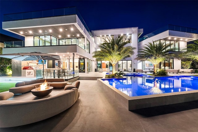 pool at twilight with an outdoor fire pit, an infinity pool, and a patio