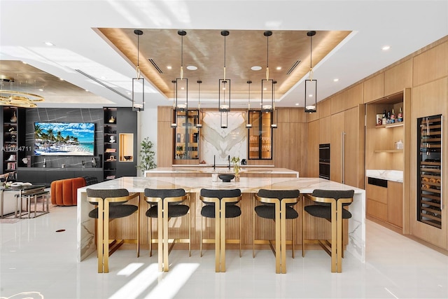 kitchen with a breakfast bar area, light stone countertops, a spacious island, a tray ceiling, and modern cabinets