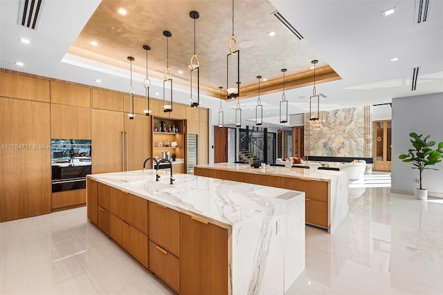 kitchen with visible vents, a raised ceiling, modern cabinets, and a large island with sink