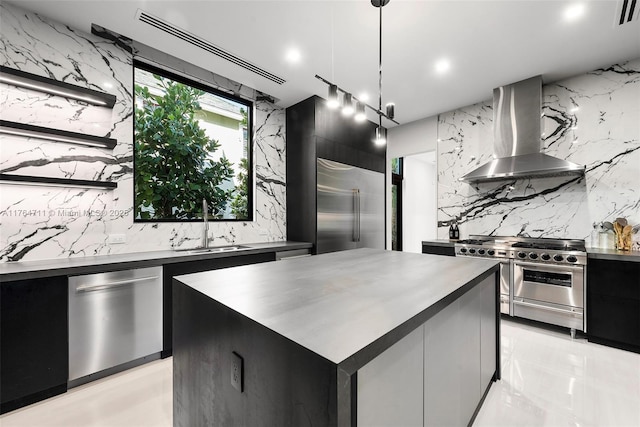 kitchen featuring dark cabinetry, high end appliances, a sink, wall chimney range hood, and modern cabinets