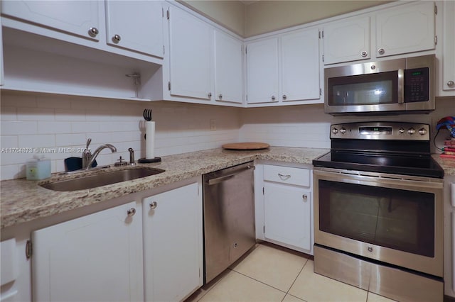 kitchen featuring backsplash, appliances with stainless steel finishes, light tile patterned flooring, white cabinets, and a sink