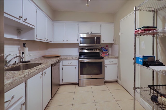 kitchen with a sink, backsplash, white cabinetry, appliances with stainless steel finishes, and light tile patterned floors