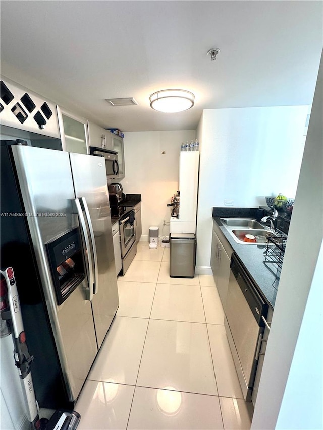 kitchen with a sink, stainless steel appliances, dark countertops, and light tile patterned floors