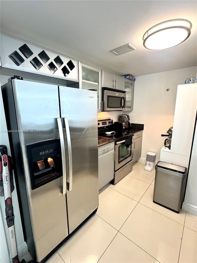 kitchen with visible vents, dark countertops, stainless steel appliances, light tile patterned floors, and glass insert cabinets