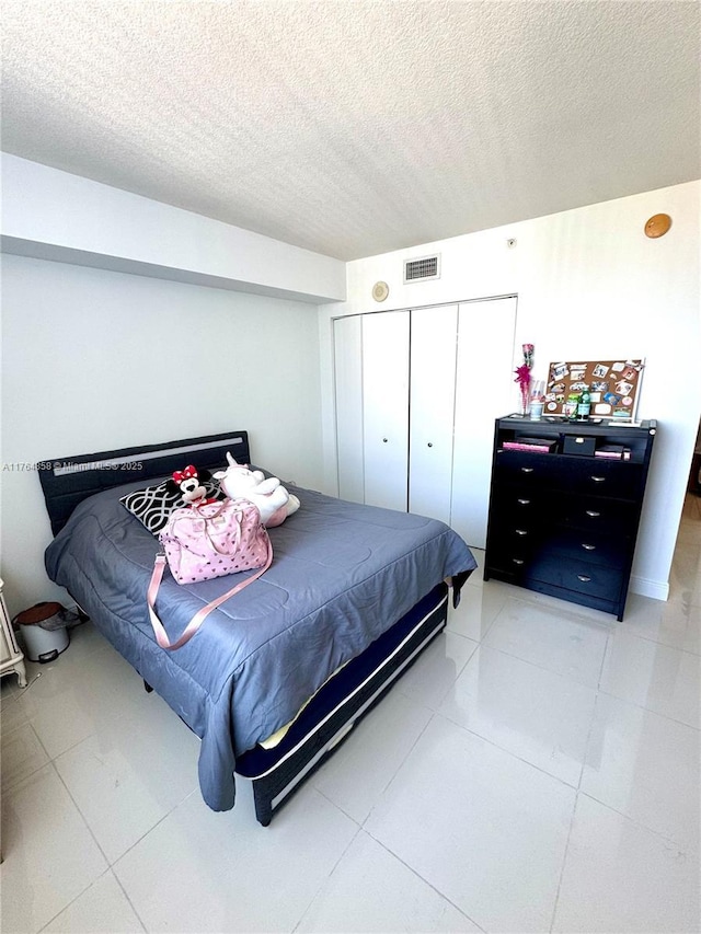 bedroom with light tile patterned floors, visible vents, a closet, and a textured ceiling