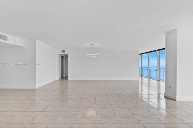 spare room with a wall of windows, light tile patterned floors, visible vents, and baseboards