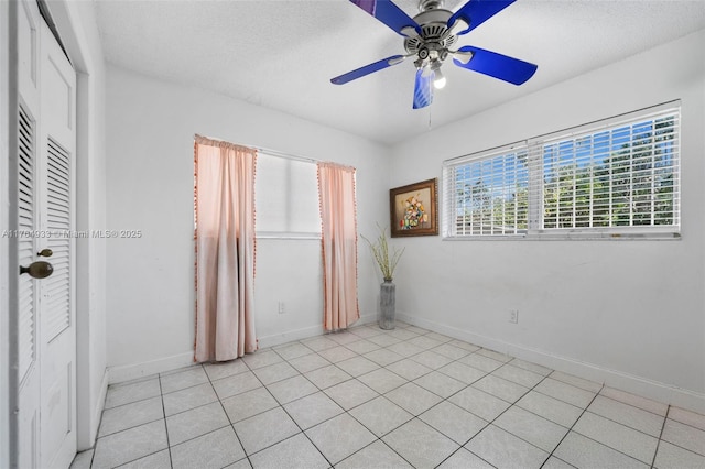 spare room featuring light tile patterned floors, ceiling fan, baseboards, and a textured ceiling