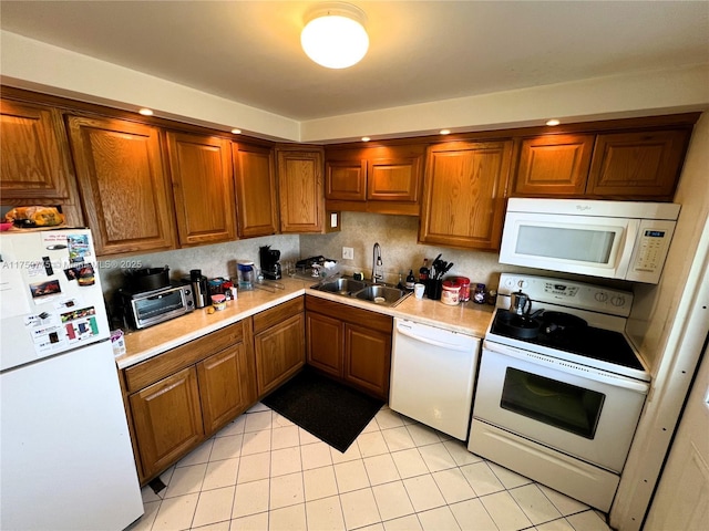 kitchen with light countertops, a sink, light tile patterned flooring, white appliances, and brown cabinetry