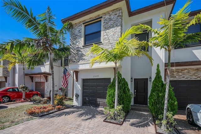 view of front of property featuring decorative driveway, stone siding, an attached garage, and stucco siding