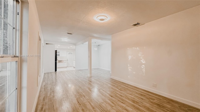 unfurnished room featuring visible vents, baseboards, a textured ceiling, and light wood finished floors