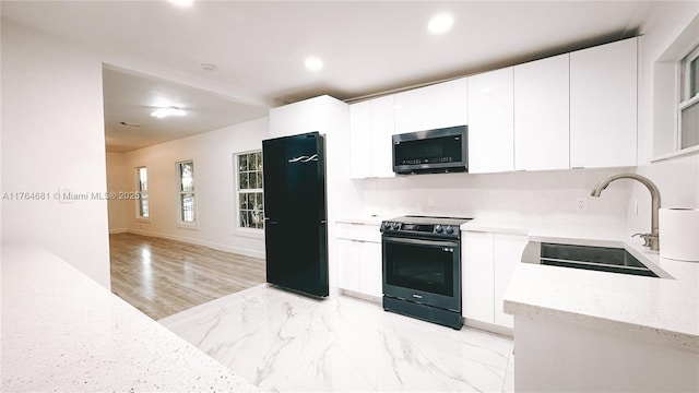 kitchen with marble finish floor, a sink, stainless steel microwave, range with electric stovetop, and freestanding refrigerator
