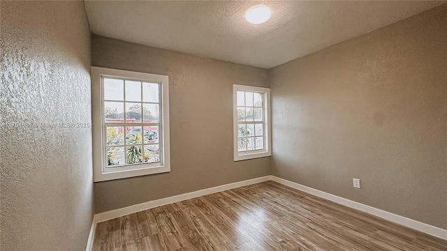empty room featuring a textured wall, a textured ceiling, baseboards, and wood finished floors