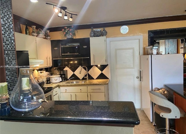 kitchen with dark stone counters, freestanding refrigerator, a sink, exhaust hood, and backsplash