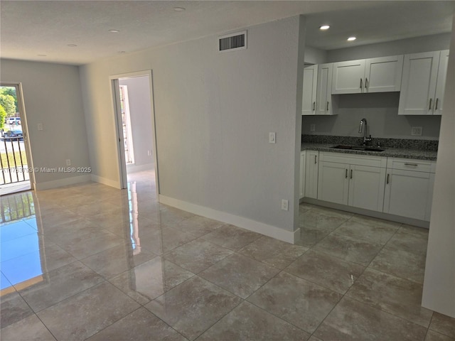 kitchen featuring white cabinets, baseboards, visible vents, and a sink