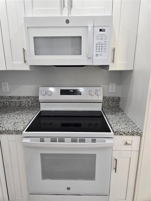 kitchen featuring light stone counters, white appliances, and white cabinets