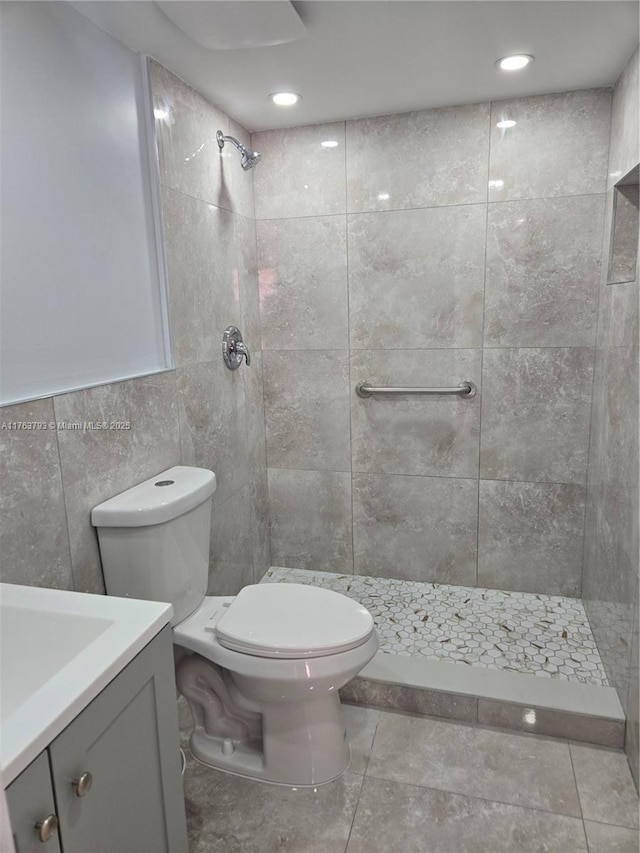 bathroom with vanity, tile walls, toilet, and a tile shower