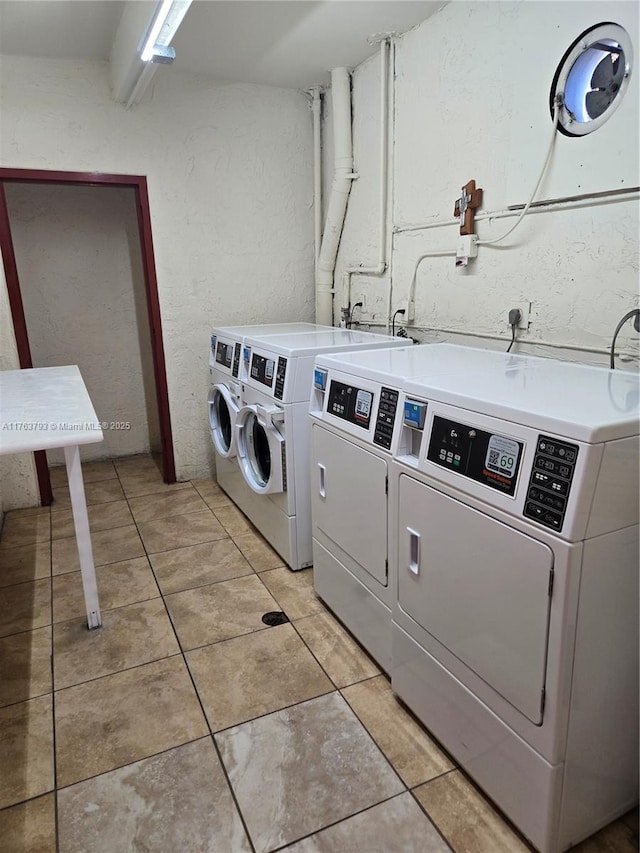 shared laundry area with light tile patterned flooring, independent washer and dryer, and a textured wall