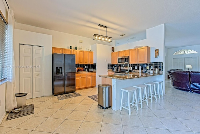 kitchen with stainless steel microwave, light tile patterned floors, black fridge, a peninsula, and a sink