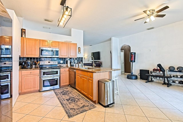 kitchen featuring a sink, stainless steel appliances, a peninsula, light tile patterned floors, and decorative backsplash