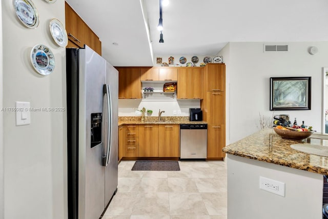 kitchen with visible vents, light stone countertops, brown cabinetry, stainless steel appliances, and a sink
