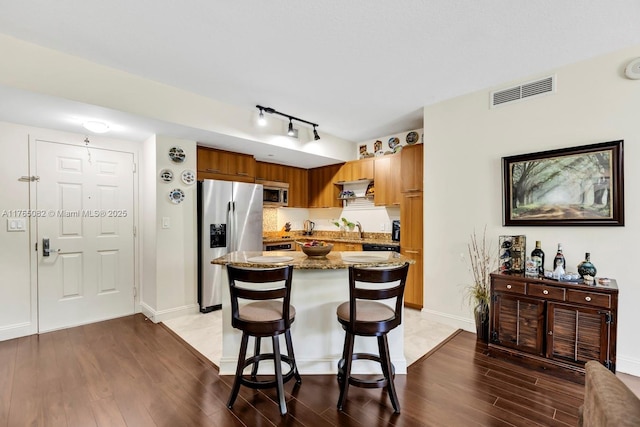 kitchen with visible vents, a center island, light stone counters, light wood-style flooring, and stainless steel appliances
