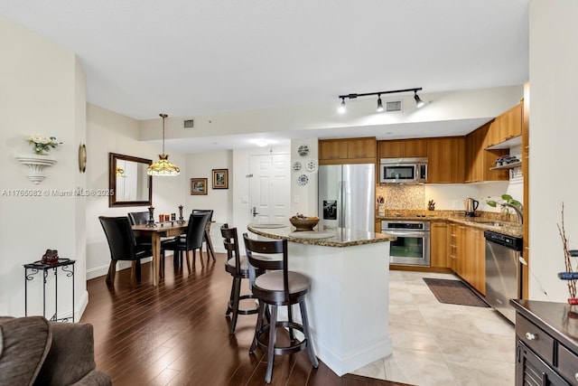 kitchen featuring dark stone countertops, a kitchen island, decorative backsplash, appliances with stainless steel finishes, and a kitchen breakfast bar