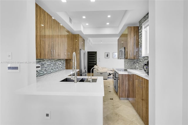 kitchen with a tray ceiling, brown cabinets, modern cabinets, and appliances with stainless steel finishes