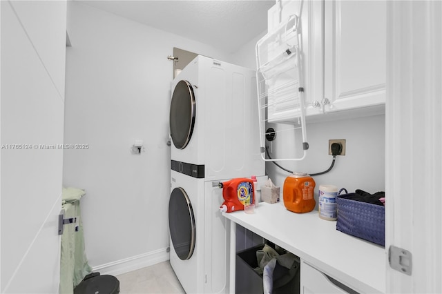 clothes washing area featuring baseboards, cabinet space, and stacked washer and dryer