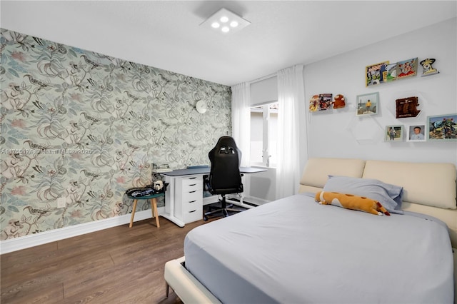 bedroom with baseboards, wood finished floors, and wallpapered walls