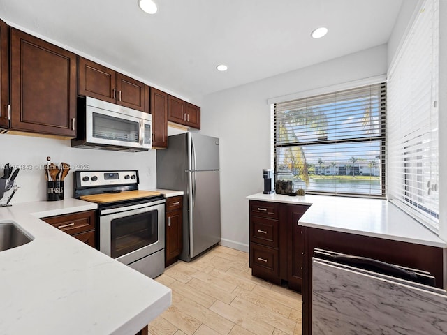 kitchen with dark brown cabinetry, recessed lighting, light wood-style floors, stainless steel appliances, and a sink