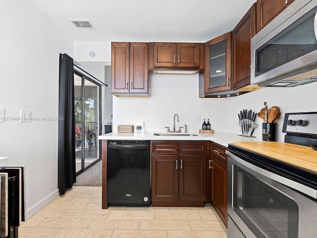 kitchen with visible vents, a sink, appliances with stainless steel finishes, light countertops, and glass insert cabinets