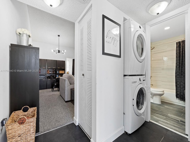 laundry area with dark tile patterned floors, laundry area, a textured ceiling, and stacked washer / drying machine