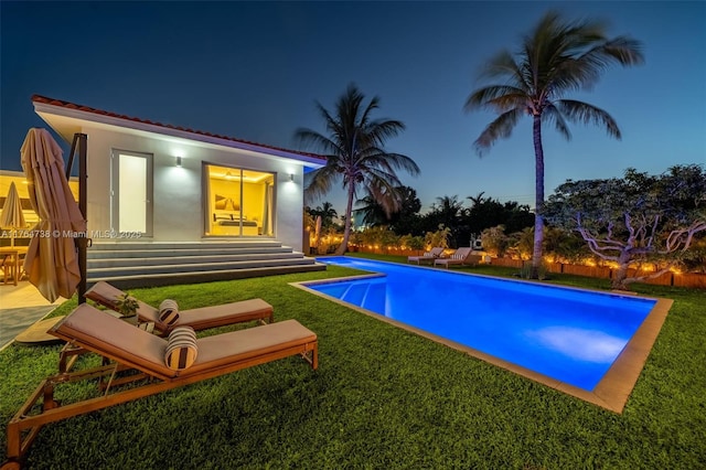 pool at night with an outdoor pool and a lawn