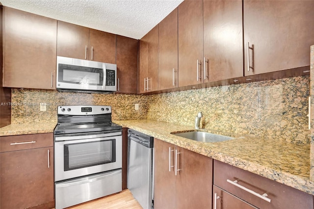 kitchen with a textured ceiling, backsplash, appliances with stainless steel finishes, and a sink