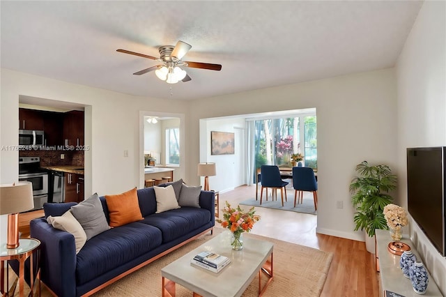 living room featuring a ceiling fan, baseboards, and light wood finished floors