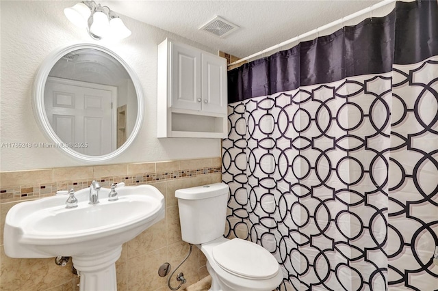 bathroom with visible vents, tile walls, toilet, a shower with shower curtain, and a textured ceiling