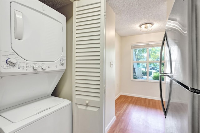 laundry area featuring a textured ceiling, light wood-style floors, stacked washer / dryer, baseboards, and laundry area