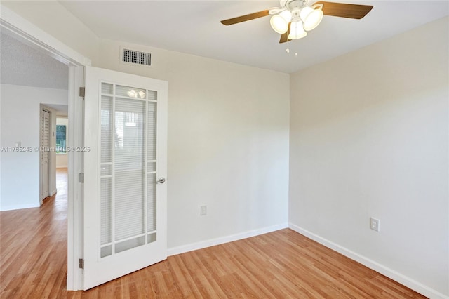 empty room featuring a ceiling fan, visible vents, light wood finished floors, and baseboards