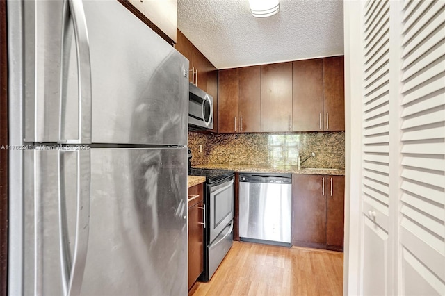 kitchen featuring a sink, decorative backsplash, stainless steel appliances, light wood-style floors, and a textured ceiling