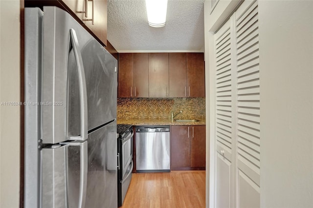 kitchen with light wood-style flooring, a sink, a textured ceiling, stainless steel appliances, and light stone countertops